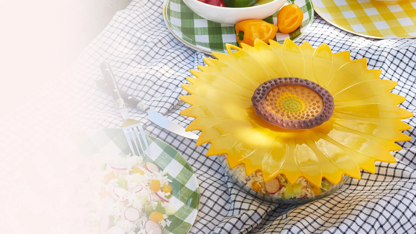 A photo of the Charles Viancin Sunflower Lid Cover on a bowl that is on a picnic table