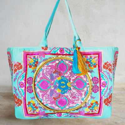 Image of the Boho Embroidered Beach Bag in the color Sea. The bag has a circular image with embroidery. Multiple colors include, teal, sea blue, berry, gold and purple. Turqoise and yellow gold tassels adorn the strap.